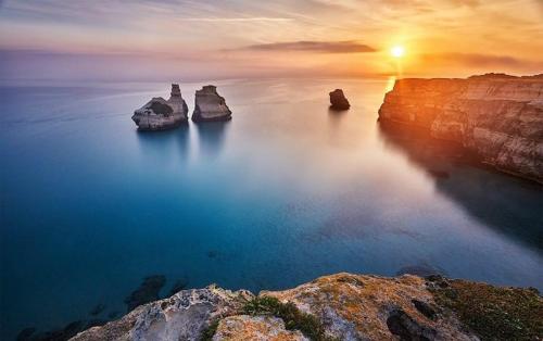 a sunset over the ocean with rocks in the water at B&B Il Villino in Torre dell'Orso