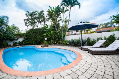a swimming pool with two chairs and an umbrella at Barbados Noosa in Noosaville