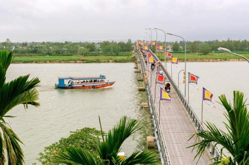 a boat on a river with flags on a bridge at B'Lan Riverside Villa in Hoi An