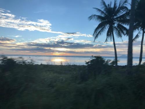 a sunset over the ocean with palm trees at Lippo Carita Beach Utara Condo Noah in Carita