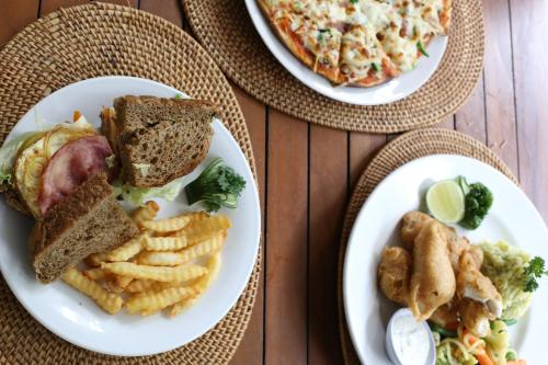 three plates of food on a table with pizza and fries at Aquarius Beach Hotel in Sanur