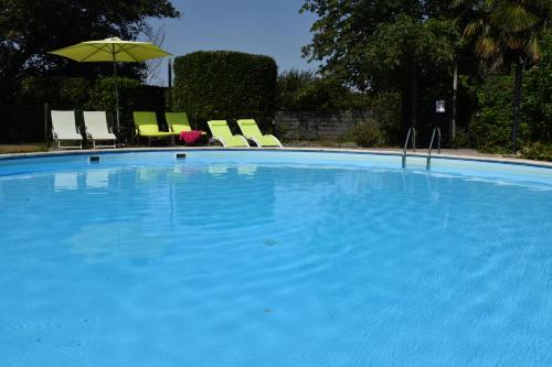 une grande piscine bleue avec des chaises et un parasol dans l'établissement Chambres d'hôtes - Dîners - Piscine - centre-ville Bergerac 5km - Domaine de Bellevue Cottage, à Lembras