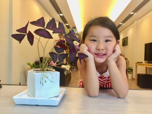 a little girl sitting at a table next to a plant at My Home N1 - BTS Ratchathewi in Bangkok