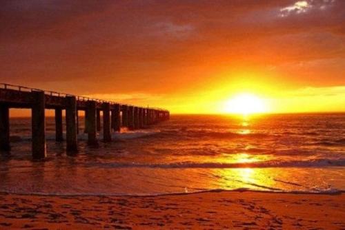a pier on the beach with the sunset in the background at Chala-Kigi Apartments in Swakopmund