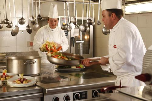 two chefs standing in a kitchen preparing food at Hotel Mirabello - Slow Hotel Benessere in Fiera di Primiero