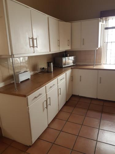 uma cozinha com armários brancos e piso em azulejo em Oasis Shanti Backpackers em Oudtshoorn