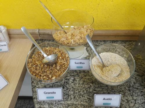 three bowls of cereal on a counter with spoons at Hotel Ideal in Londrina