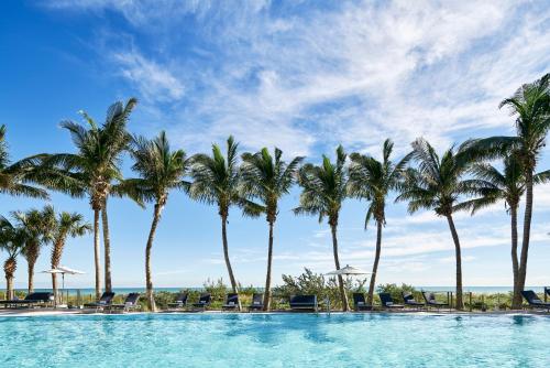 a pool with palm trees and chairs on the beach at Carillon Miami Wellness Resort in Miami Beach
