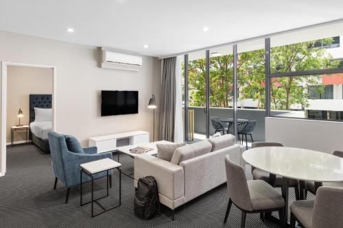 um quarto de hotel com um sofá, uma mesa e cadeiras em Meriton Suites Waterloo em Sidney