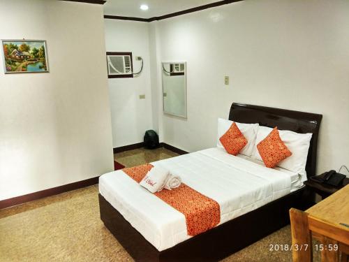 Schlafzimmer mit einem Bett mit orangefarbenen und weißen Kissen in der Unterkunft Bicotels Hotel in Batangas City