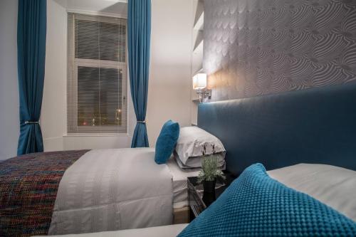 a bedroom with two beds with blue curtains and a window at West Highland Apartments Milngavie - The Lomond in Milngavie