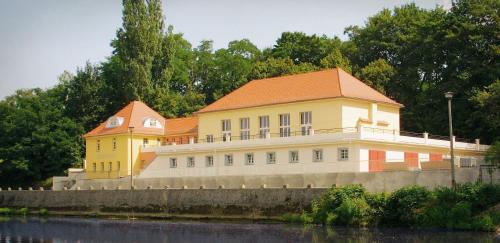 a yellow building with an orange roof next to a river at Pension Bootshaus in Weißenfels
