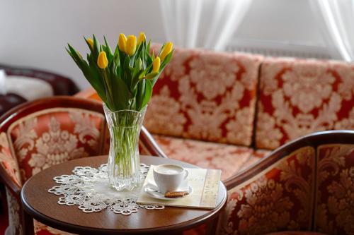 a vase of yellow flowers on a table with a cup at Dworek Vesaria in Lublin