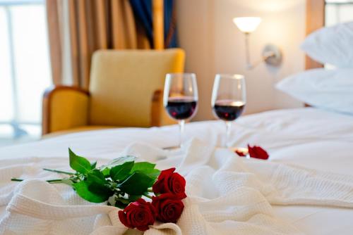 two glasses of wine and roses on a bed at Leonardo Hotel Jerusalem in Jerusalem