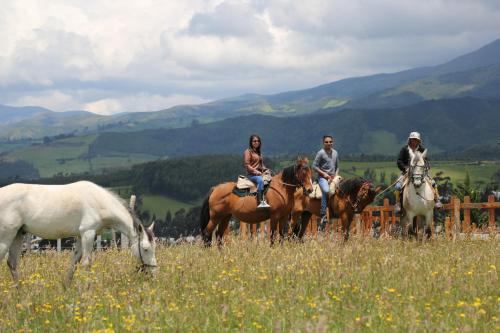 three people riding horses in a field with a goat at Hosteria Loma Larga Cayambe in Cayambe