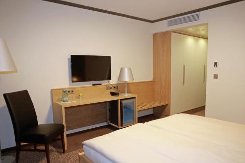 ein Hotelzimmer mit einem Bett und einem Schreibtisch mit einem TV in der Unterkunft Hotel Ratsstuben in Rehden