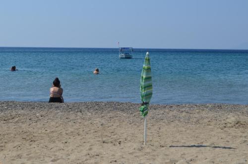 a green and white umbrella on the beach with people in the water at Mulka Hotel in Ayvalık