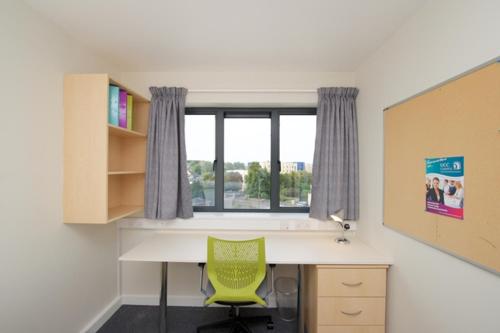 Habitación con ventana y escritorio con silla verde. en University Hall Apartments - UCC Summer Beds en Cork