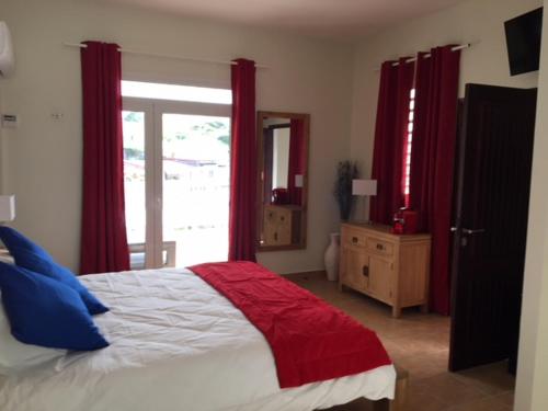 a bedroom with a bed with red curtains and a window at Residence Hôteliere Hurlevent in Grande Anse