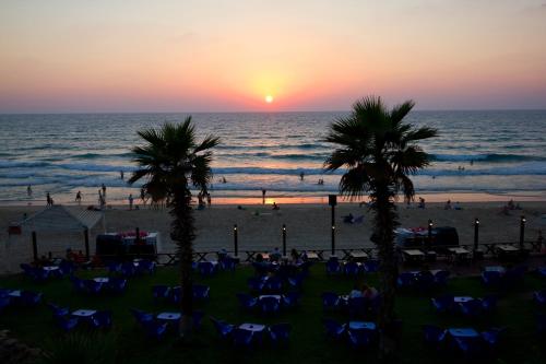 a sunset at the beach with palm trees and chairs at The Royal Penthouse in Bat Yam