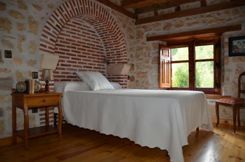 a bedroom with a white bed and a brick wall at Casa Rural El Covanchón in Prádena