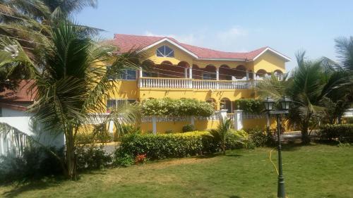 una casa gialla con palme di fronte di Coconut Pointe Villa & Beach Resort a Prampram
