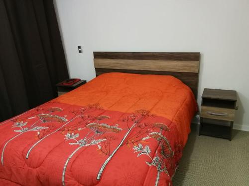 a bed with an orange comforter and a wooden headboard at Departamento santiago in Santiago
