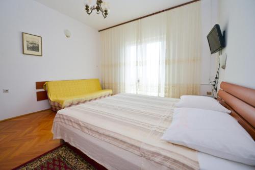 a bedroom with a large bed and a yellow chair at Apartman Nikodem in Novalja