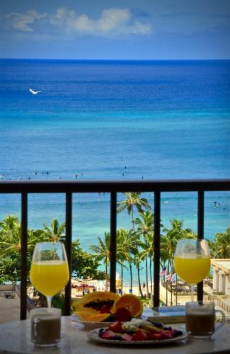 a table with two glasses of orange juice and the ocean at Jenny's Cottage Waikiki in Honolulu