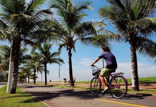 a man riding a bike down a street with palm trees at Apartamento Praia Grande in Praia Grande