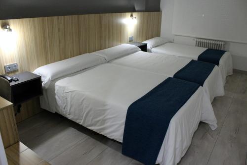 two beds in a hotel room with white and blue sheets at Hotel Altiana in Ourense