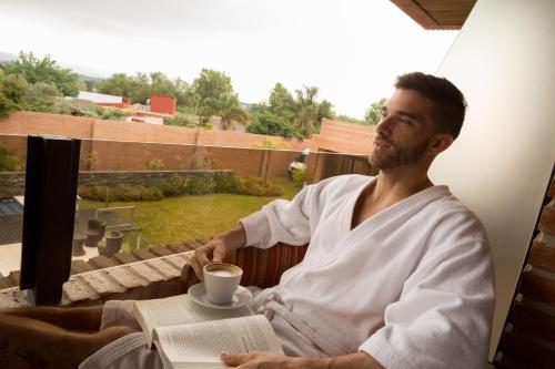 a man sitting in a chair with a book and a cup of coffee at Neper Hotel in Cordoba