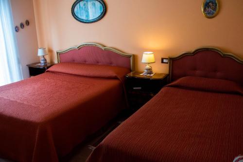 two beds in a hotel room with red sheets at B&B Villa Liliya in Fiumefreddo di Sicilia