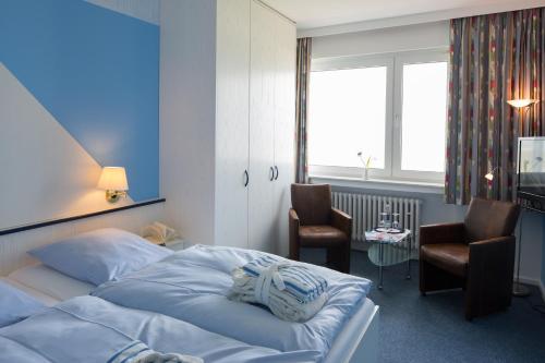 a bedroom with a bed and two chairs and a window at Hotels Haus Waterkant & Strandvilla Eils in Norderney