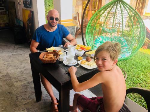 a man and a young boy sitting at a table eating breakfast at St CLAIRE'S GREEN Negombo Hotel & Hostels in Negombo