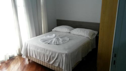 um quarto com uma cama com lençóis brancos e almofadas em Rocha's Hotel em Guarapuava