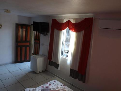 Habitación con una ventana con cortinas rojas y TV. en Hotel Anjo Gabriel, en Penha