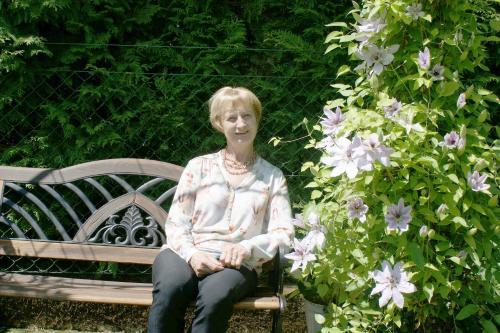 an older woman sitting on a bench next to flowers at Gästehaus Struggl in Steindorf am Ossiacher See
