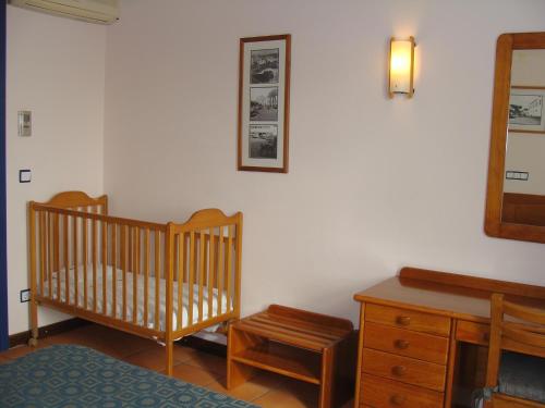 a room with a crib and a dresser and a mirror at Apartamentos Turisticos Verdemar in Horta