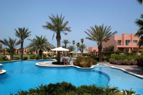 a large swimming pool in a resort with palm trees at Seashell Julai'a Hotel & Resort Family resort in Al Qulay‘ah