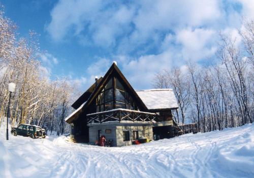 a log cabin in the snow with a car parked in front at Pension Gooseberry in Furano