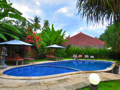 a pool in a yard with chairs and umbrellas at Suka Sari Cottages in Pemuteran