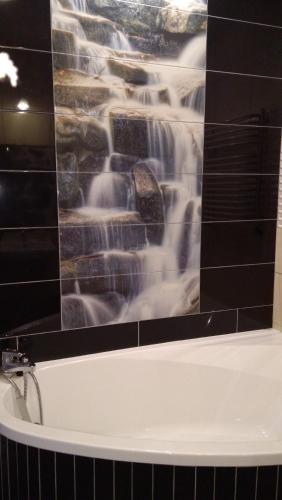 a bath tub with a waterfall mural on a bathroom wall at Zajazd Eljan-Centrum Noclegowe in Olsztyn