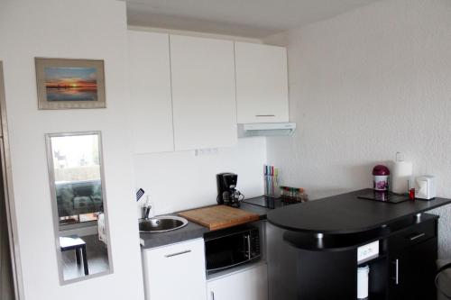 a small kitchen with white cabinets and a black counter top at Studio 237 Port Camargue, Piscine, Climatisation, 2 personnes in Le Grau-du-Roi