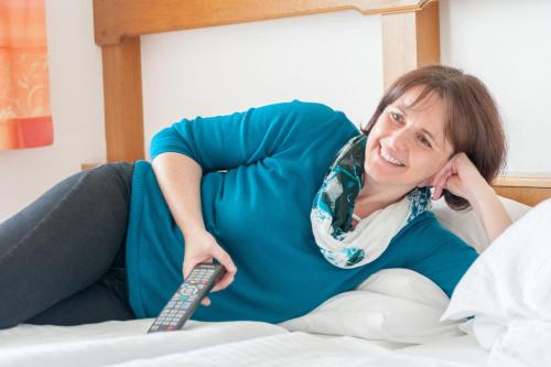 a woman laying on a bed holding a remote control at Florianihof in Miesenbach