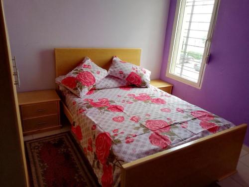 a bedroom with a bed with a floral quilt and a window at Cozy Appartement in Douar Ben Chellal