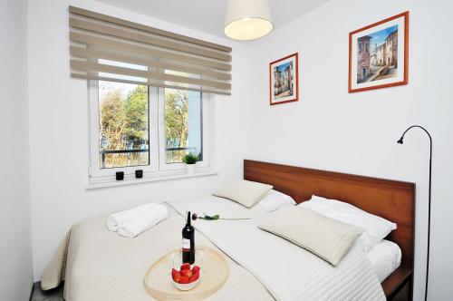 a white bedroom with a bed with a bottle of wine at Dwie Sosny Apartament 38 - Perła in Ustronie Morskie