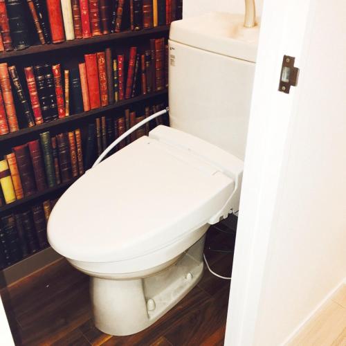 a bathroom with a toilet in front of a book shelf at Guest House Fukuoka W302 in Kasugabaru