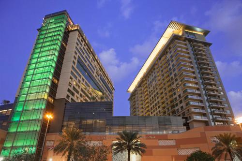 two tall buildings with palm trees in front of them at Swissôtel Living Al Ghurair Centre Dubai in Dubai