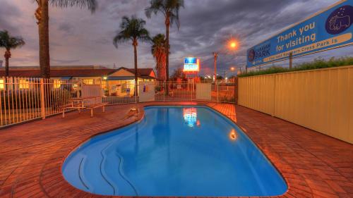ein blauer Swimmingpool mit Zaun und Palmen in der Unterkunft Dubbo Midstate Motor Park in Dubbo